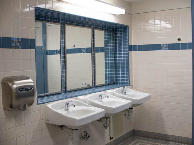 Public restroom with three wall-hung sinks under a window and a stainless hand dryer on white tile
