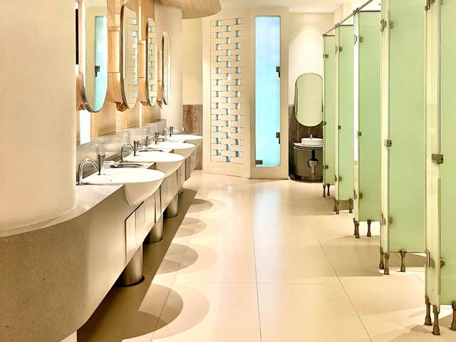 Bright commercial restroom with a light tile floor, round mirrors and frosted partitions