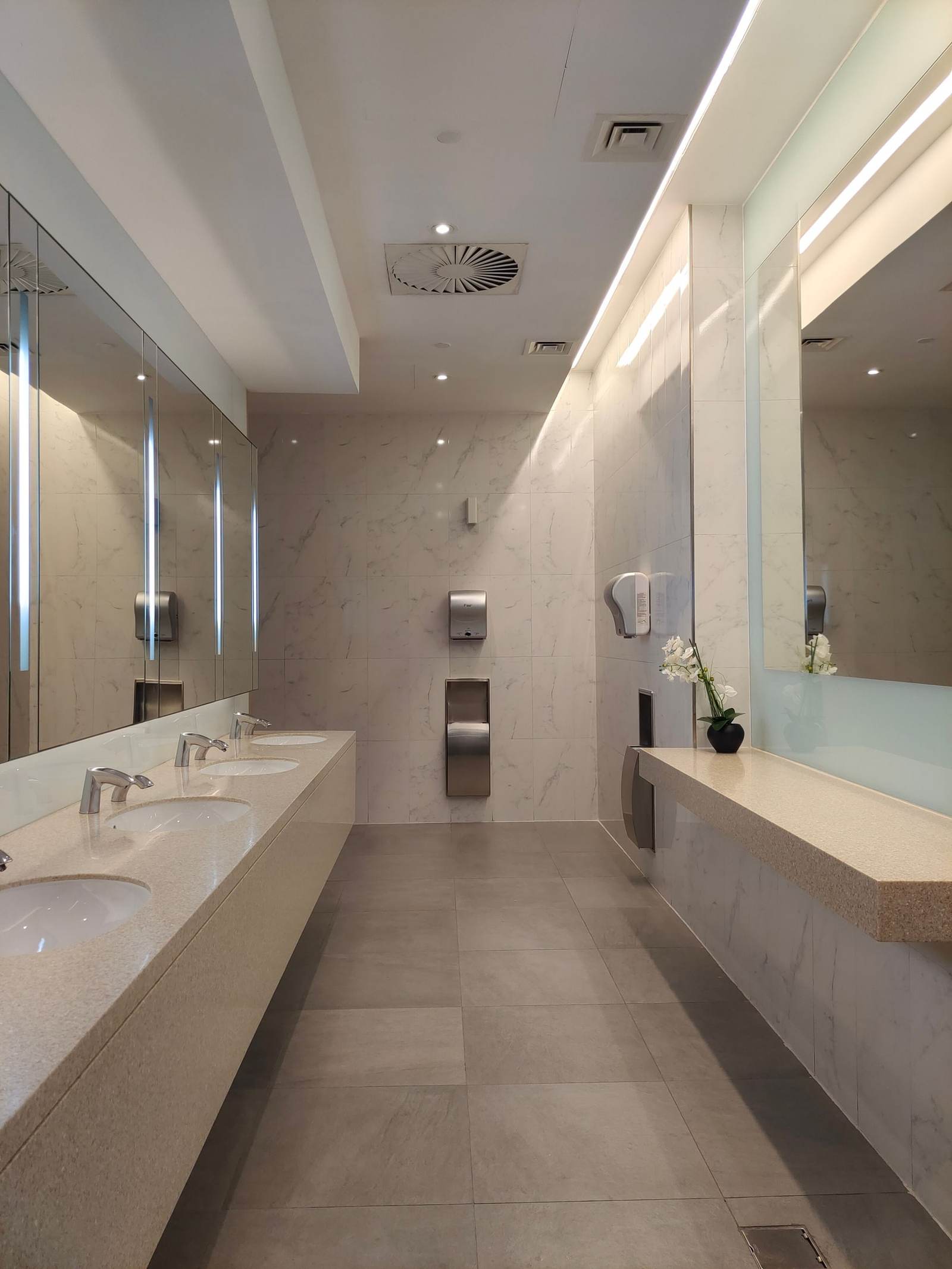 Rebuilt commercial restroom with a long stone counter, sensor faucets, and wall-mounted dryers
