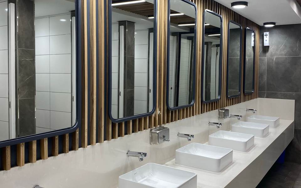 Commercial restroom with a long white counter of vessel sinks under framed mirrors
