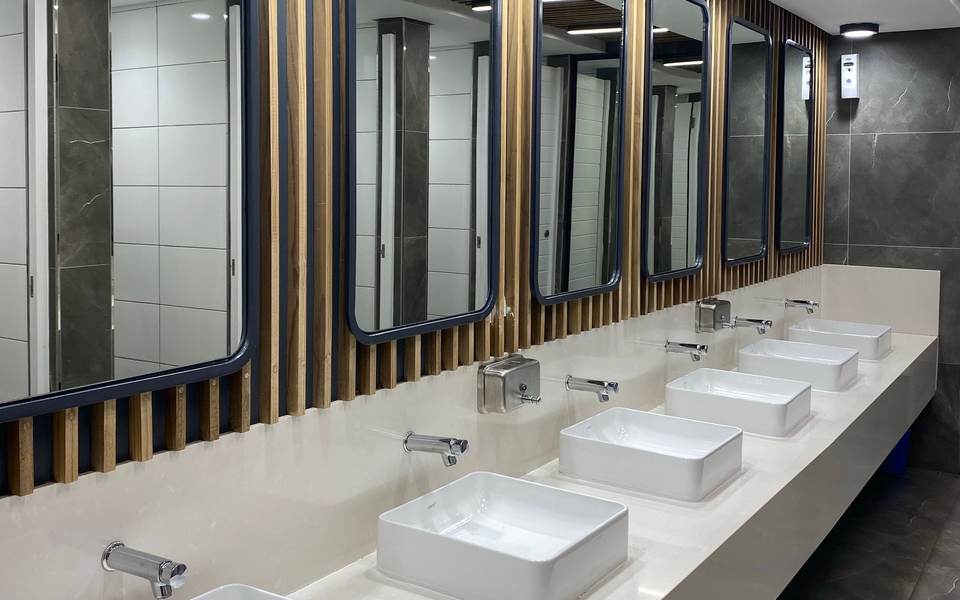 Commercial restroom with a long counter of white vessel sinks under mirrors framed by wood slats