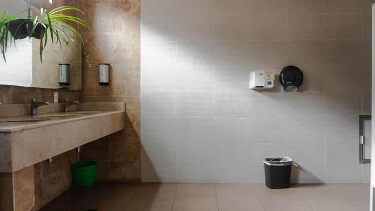 Restroom with a stone counter, wall-mounted soap dispensers and a paper towel dispenser on tiled walls