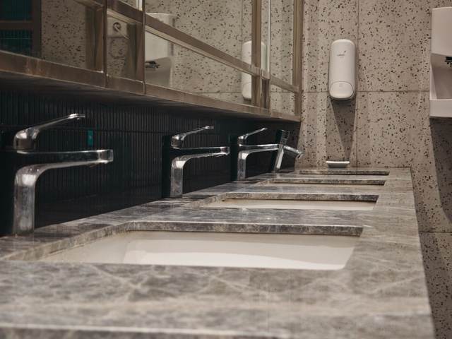 Row of stainless faucets along a commercial restroom counter