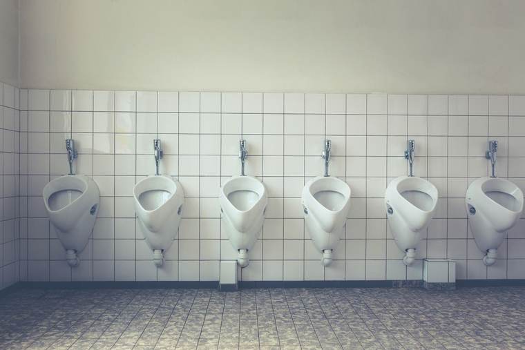 Row of white urinals with flush valves on a white tile wall