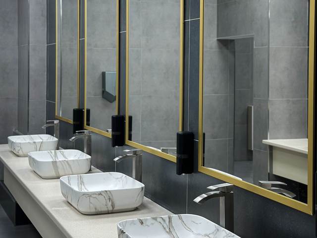Commercial restroom with marble-look vessel sinks, brass-framed mirrors, and dark gray tile