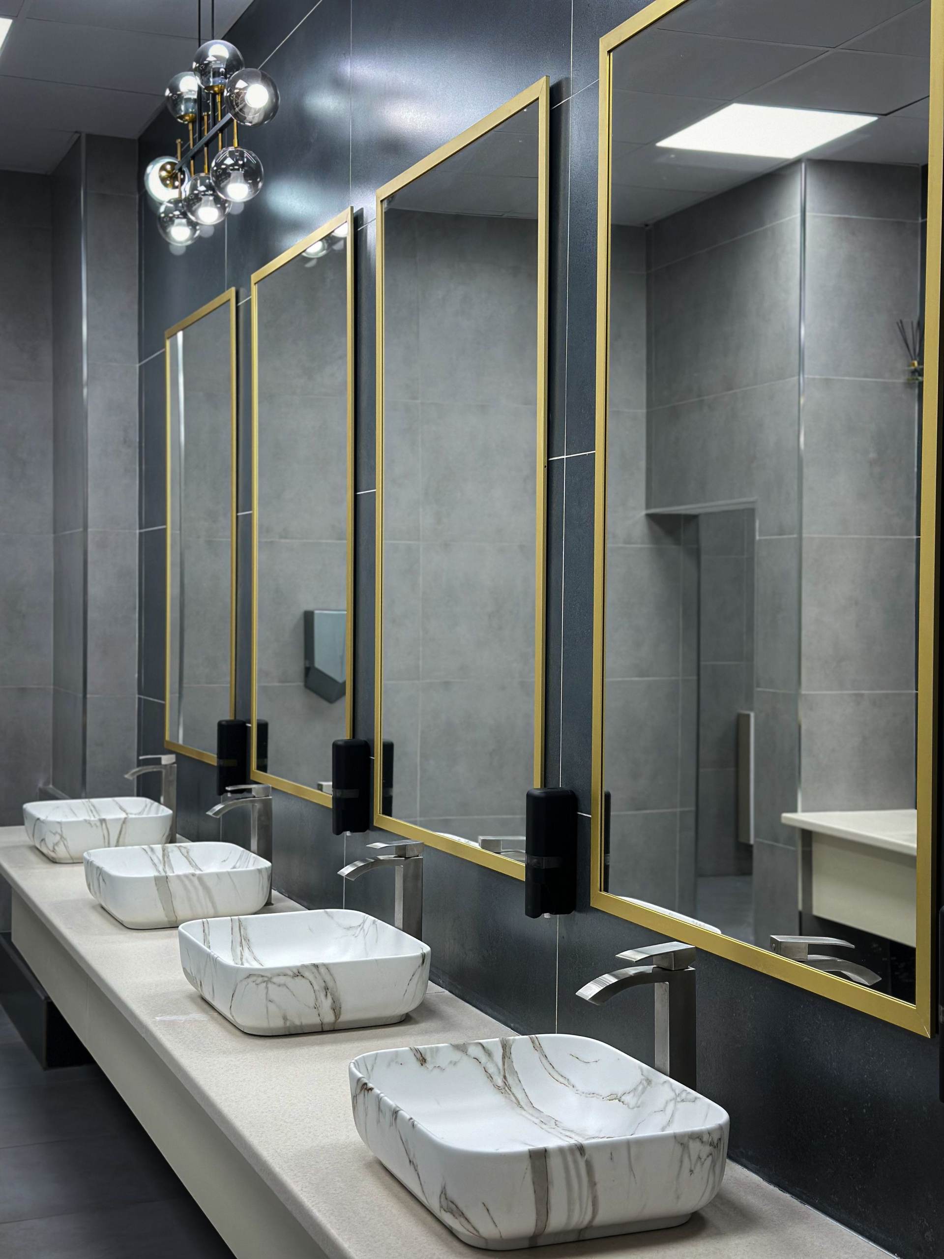 Commercial restroom counter with marble-look vessel sinks, tall faucets and brass-framed mirrors