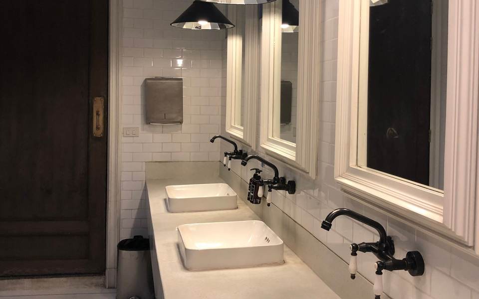 Restroom with a row of white vessel sinks on a long counter under pendant lights and framed mirrors