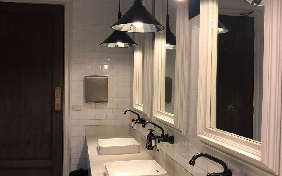 Restroom with three vessel sinks on a stone counter, pendant lights, white subway tile and a dark wood door