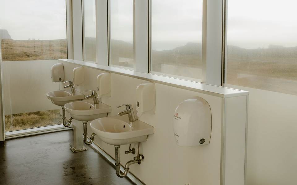 Restroom with a row of wall-mounted sinks under tall windows and a hand dryer on the wall