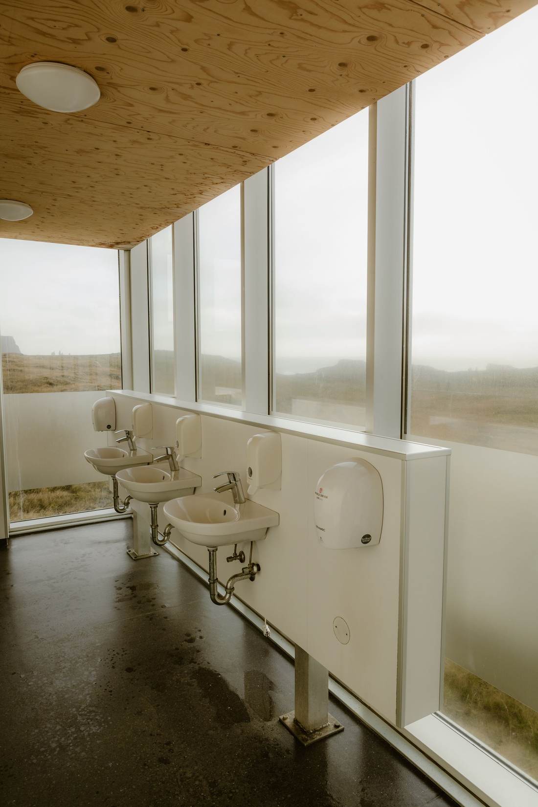 Public restroom with wall-hung sinks under tall windows and a wall-mounted hand dryer
