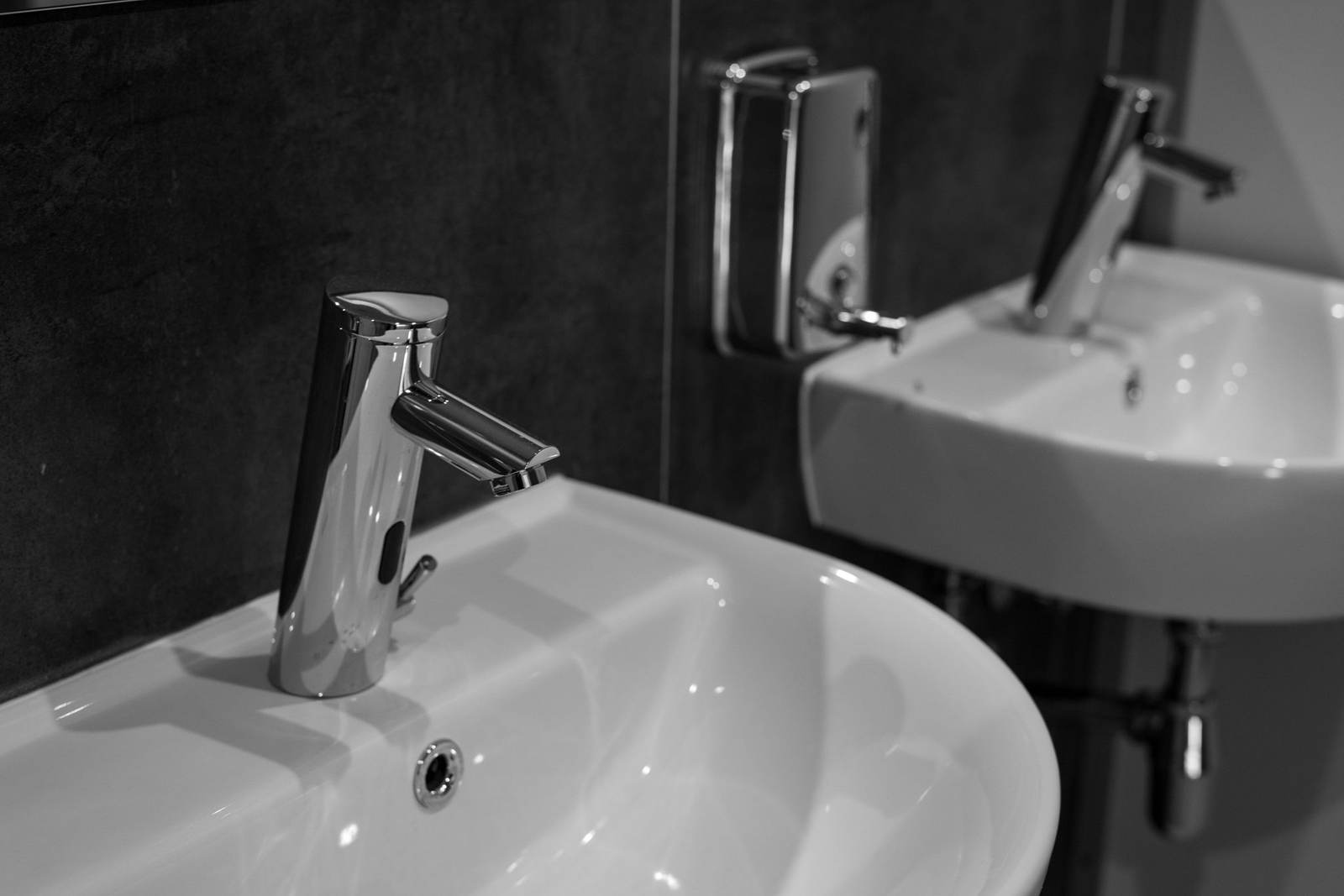 Chrome sensor faucet over a white wall-hung sink beside a soap dispenser