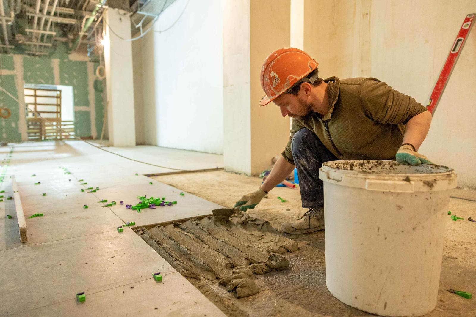 Tile installer in a hard hat spreading mortar for floor tile in a commercial renovation