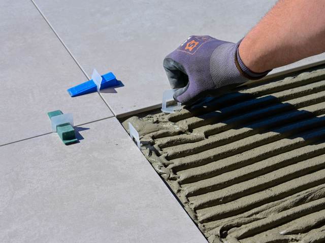 Gloved hand setting leveling clips between large floor tiles over notched mortar