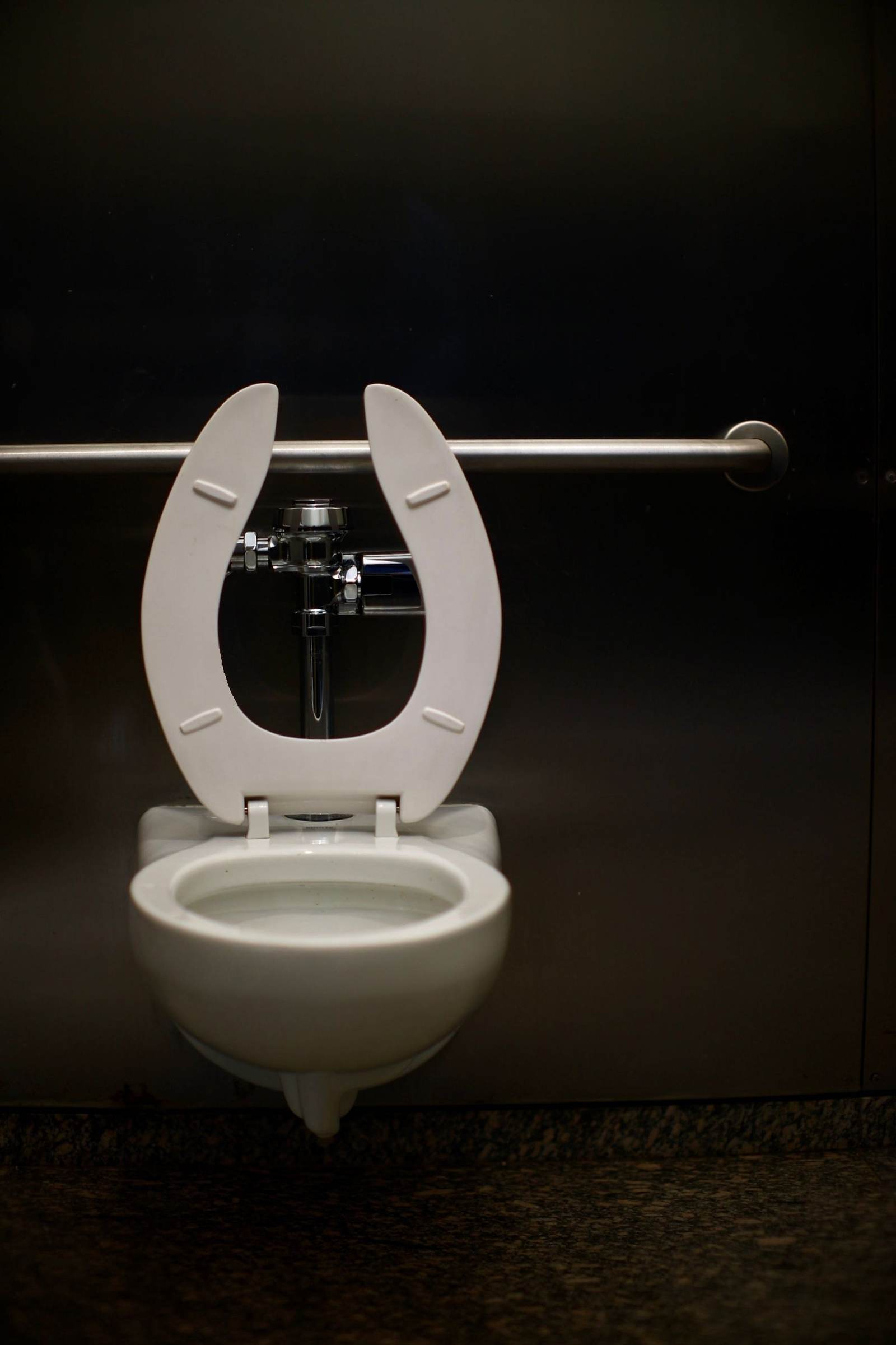 Commercial toilet with an open-front seat and a stainless grab bar on a dark wall