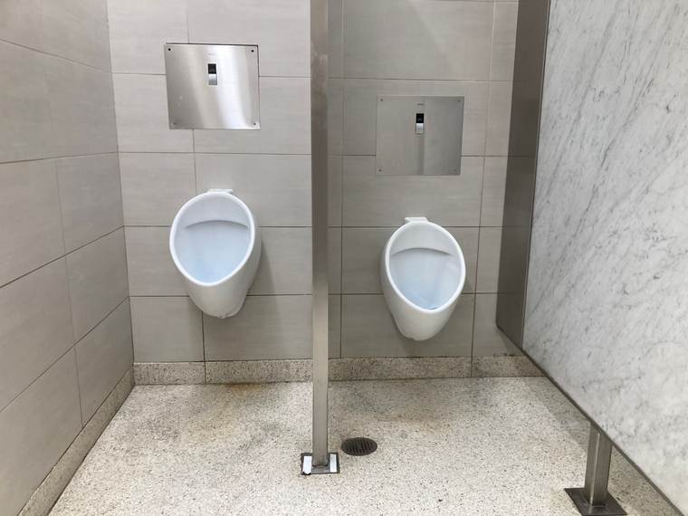 Two wall-hung urinals with sensor flush valves separated by a divider on a marble-look wall