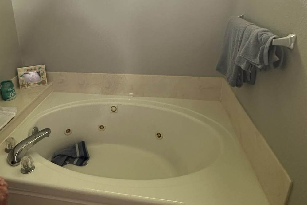 Before: a corner jetted tub with a tiled surround under a transom window, in a Glenpool bathroom we turned into a roll-in shower
