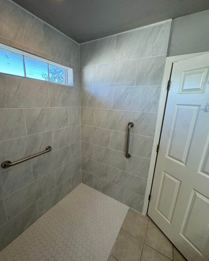 Curbless roll-in shower with large gray tile, a white hex floor and grab bars under a transom window, in a Glenpool home