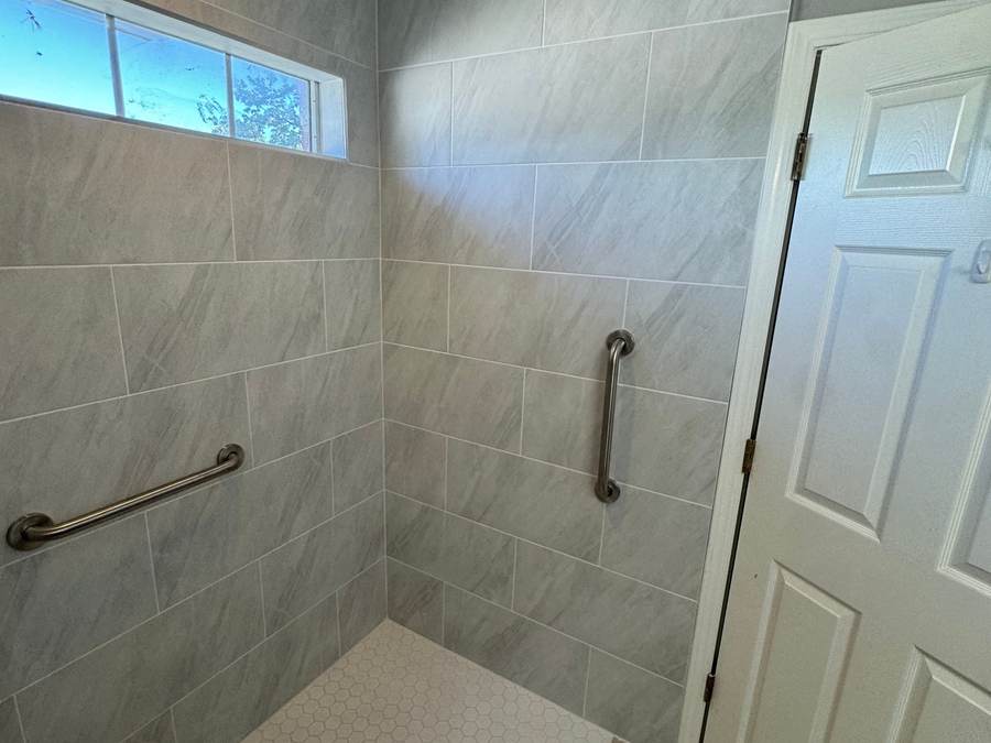 Curbless roll-in shower with large gray tile, a white hex floor and grab bars under a transom window, in a Glenpool home