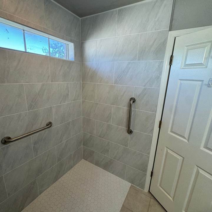 A curbless roll-in shower with large gray tile under a transom window