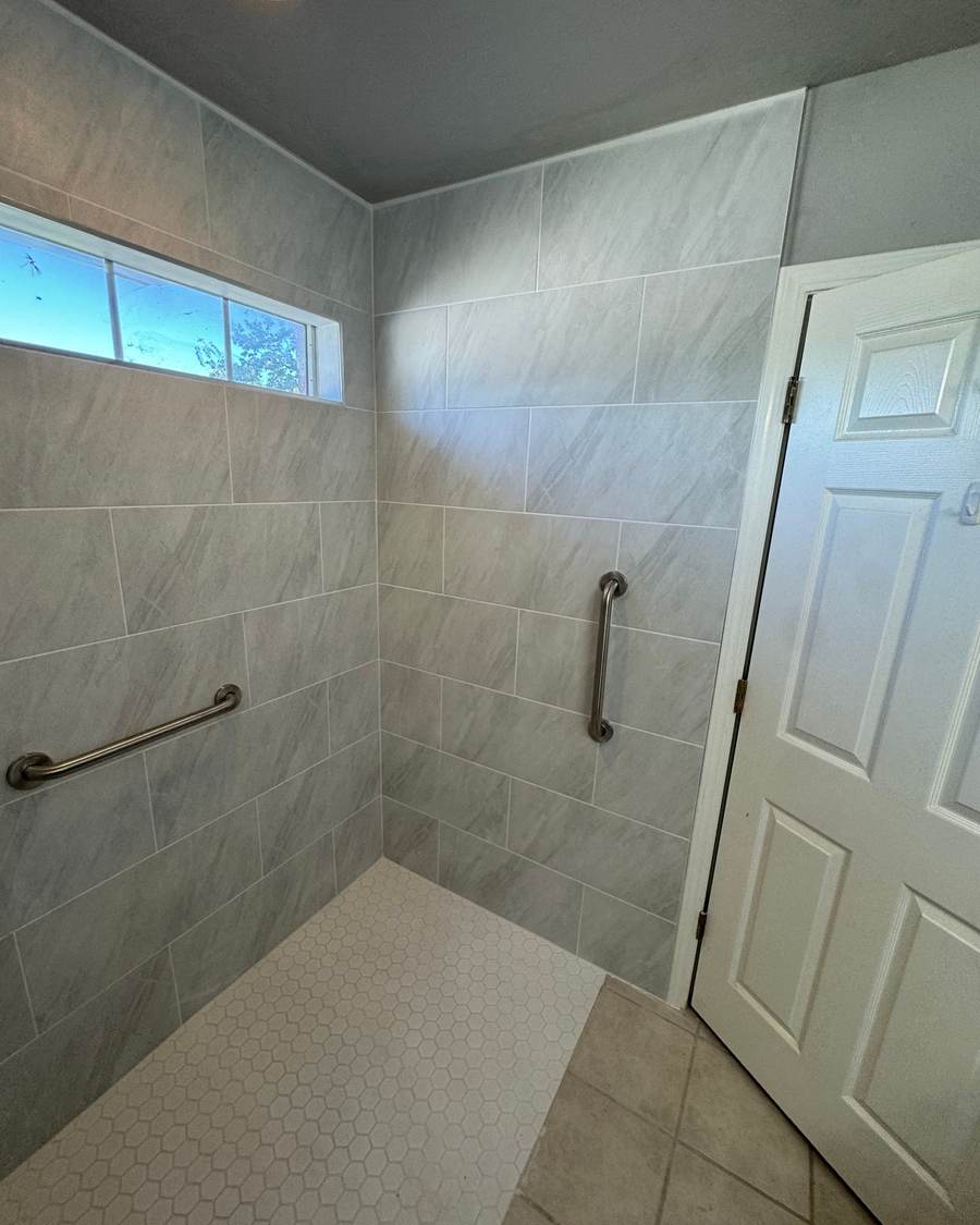 After: a curbless roll-in shower with grab bars under the same transom window in Glenpool
