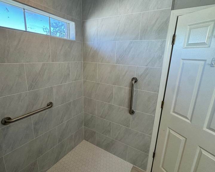 Curbless roll-in shower with large gray tile, a white hex floor and grab bars under a transom window, in a Glenpool home