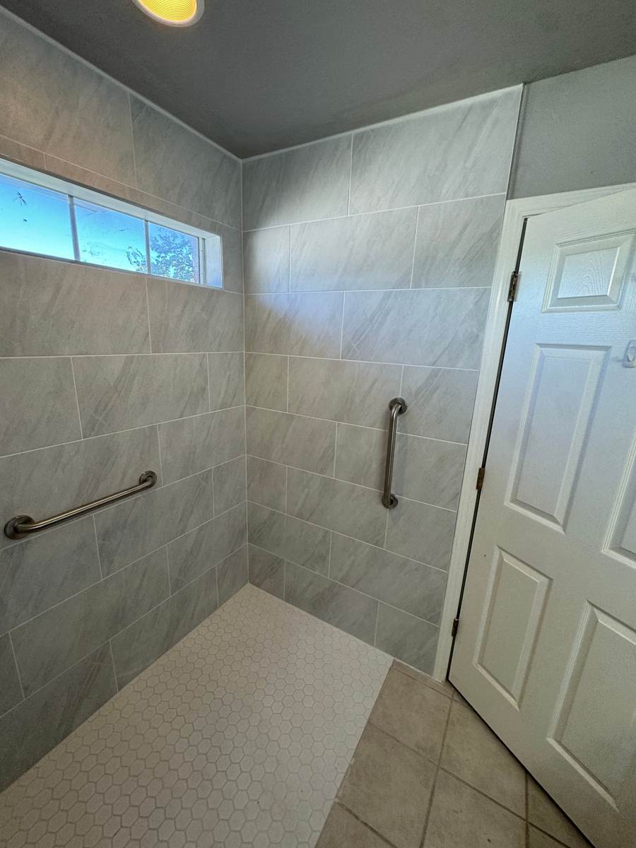 After: a curbless roll-in shower with grab bars under the same transom window in Glenpool