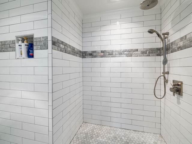 Curbless shower with no step at the entry, white subway tile, and a hand shower on the wall