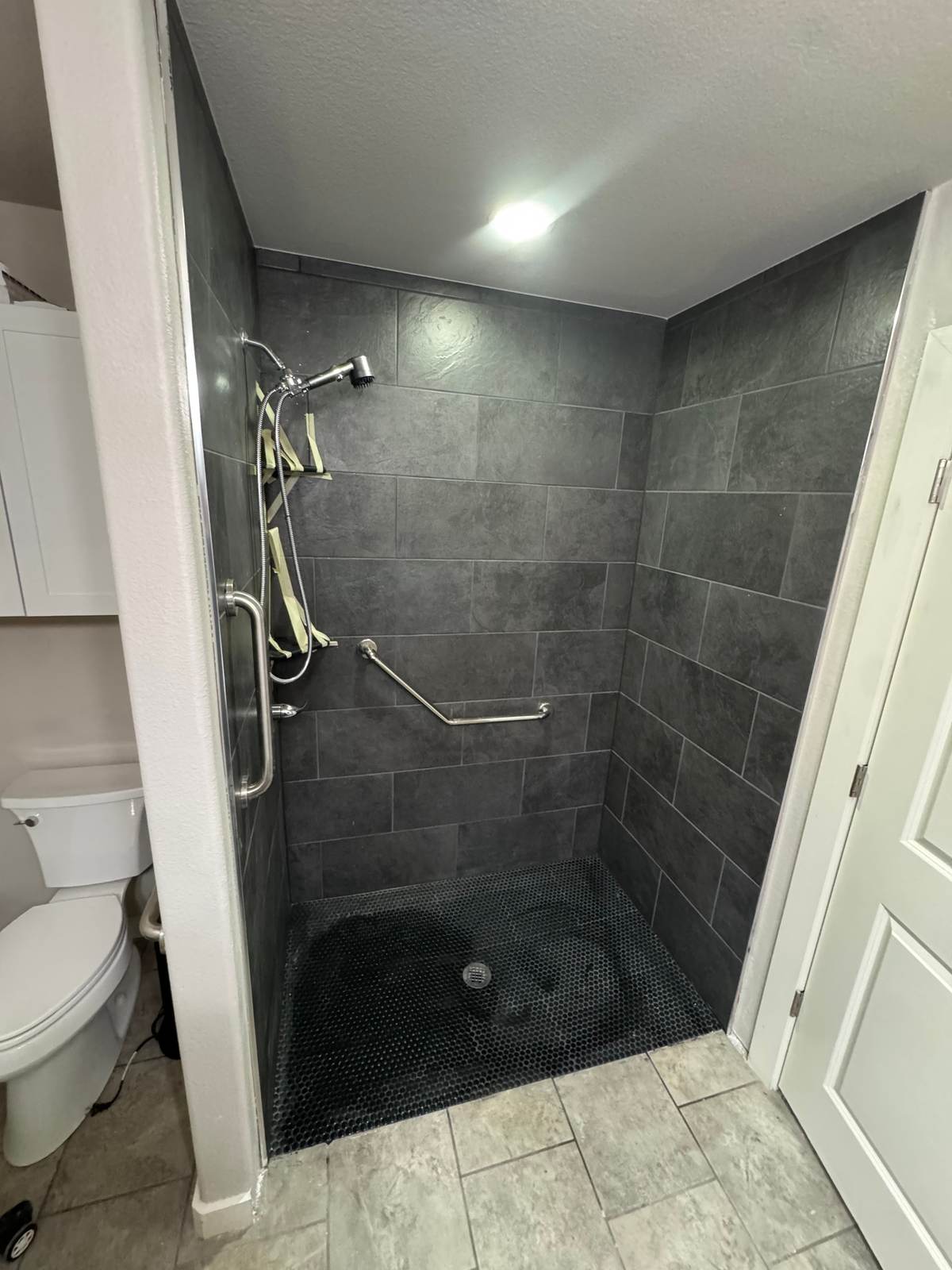 The Bixby walk-in shower beside the toilet, with grab bars and a dark mosaic floor