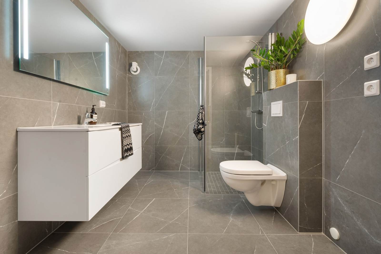 Curbless walk-in shower behind one glass panel, gray porcelain tile running level from the bathroom floor into the shower