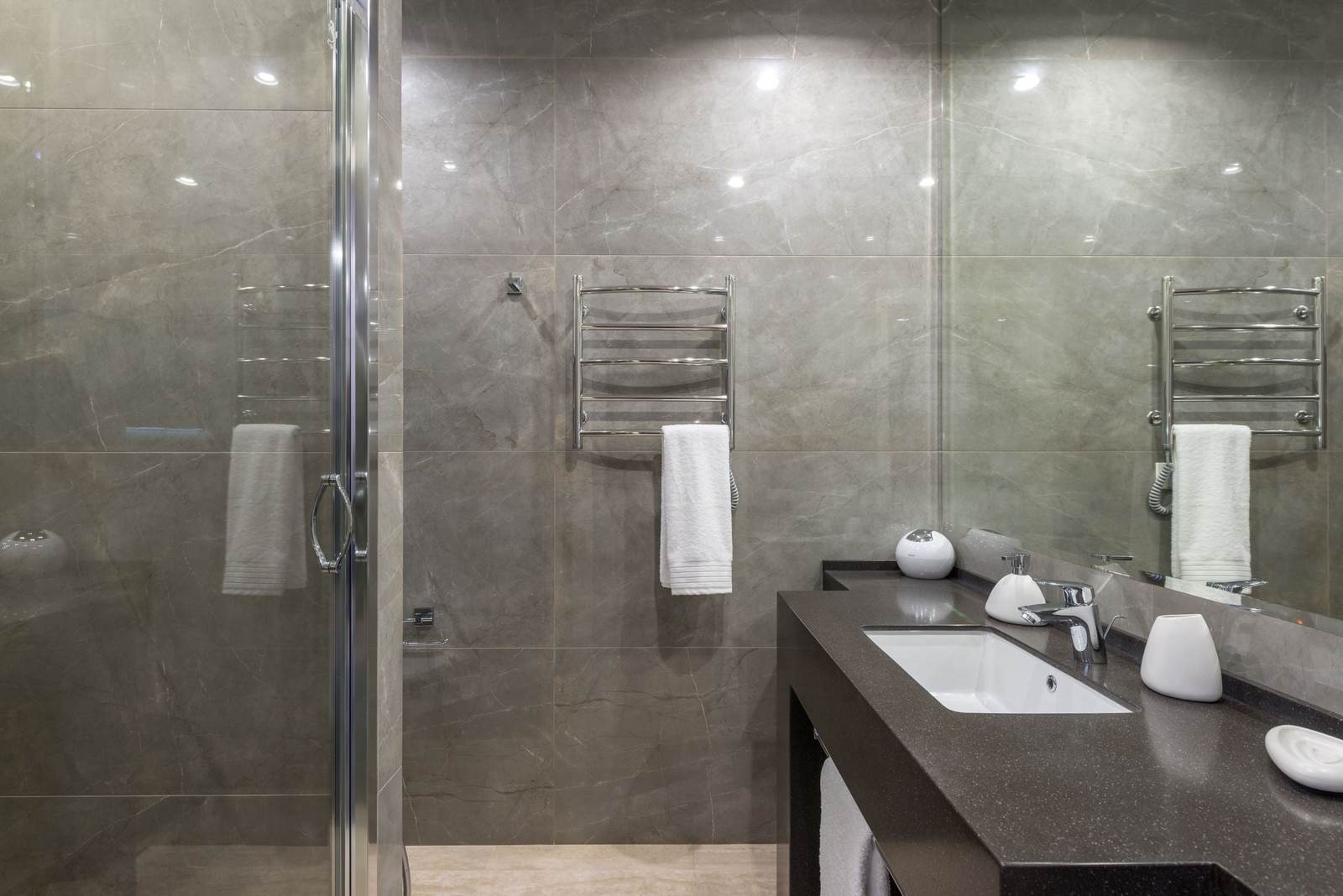 Curbless walk-in shower with gray porcelain tile and a frameless glass door, the floor running level into the shower beside a dark vanity