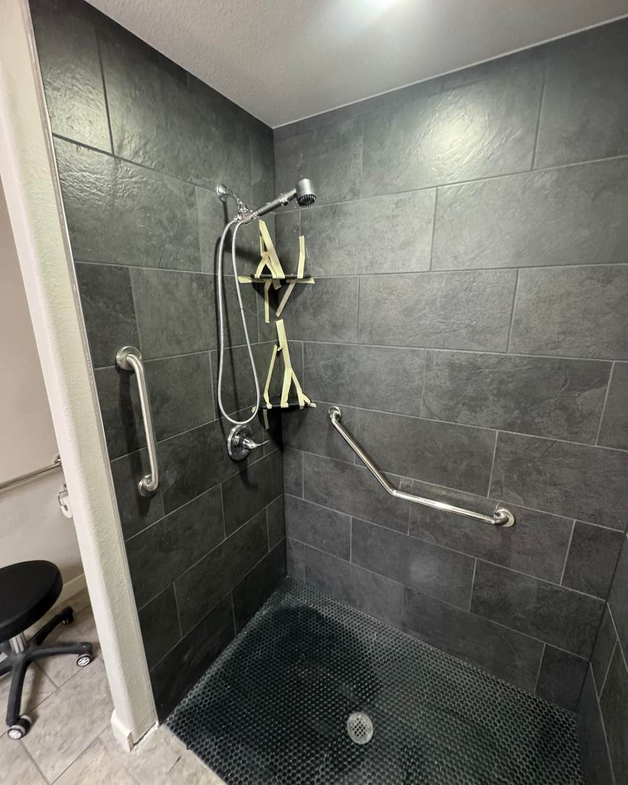 After: a tiled walk-in shower with slate-look tile, a dark mosaic floor and grab bars in the same Bixby bathroom