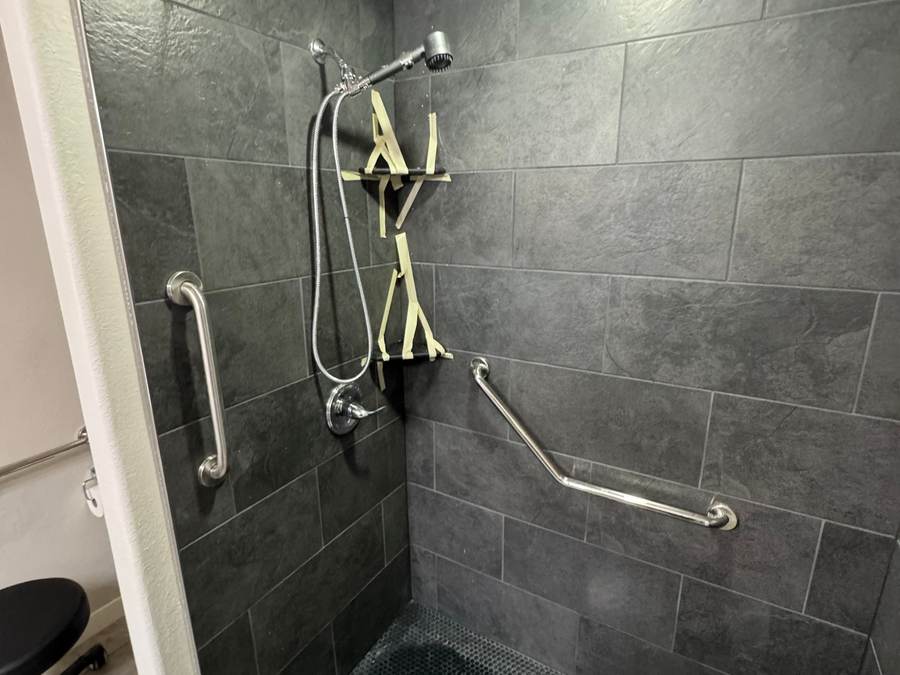 Tiled walk-in shower with slate-look tile, a dark mosaic floor and grab bars in a Bixby master bathroom