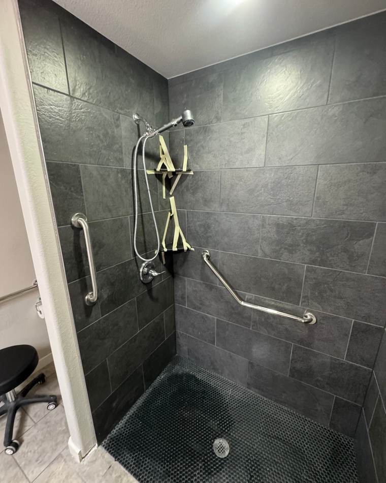 After: a curbless walk-in shower with slate-look tile, a dark mosaic floor and grab bars