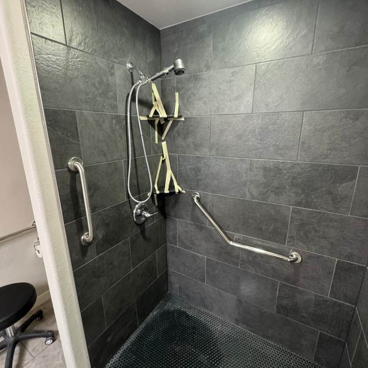 Tiled walk-in shower with slate-look tile, a dark mosaic floor and grab bars in a Bixby master bathroom