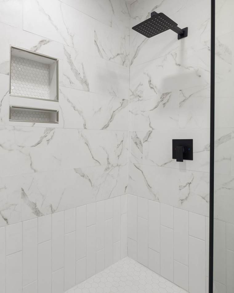Marble-look porcelain shower with a recessed two-shelf niche, a square matte black shower head and valve, white subway tile below and a glass panel