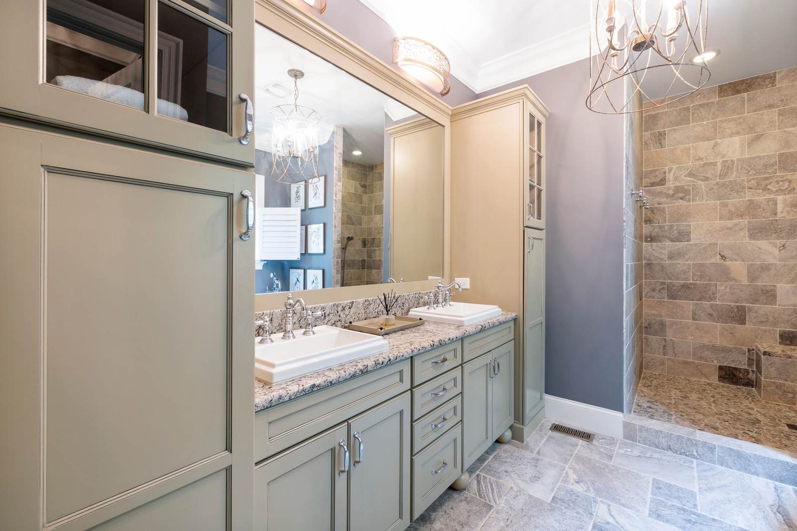 Doorless walk-in shower in stone-look tile with a pebble floor, past a double vanity in a primary bathroom