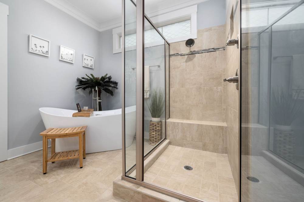 Glass shower enclosure with a brushed metal frame on a tiled curb, and a tiled bench inside