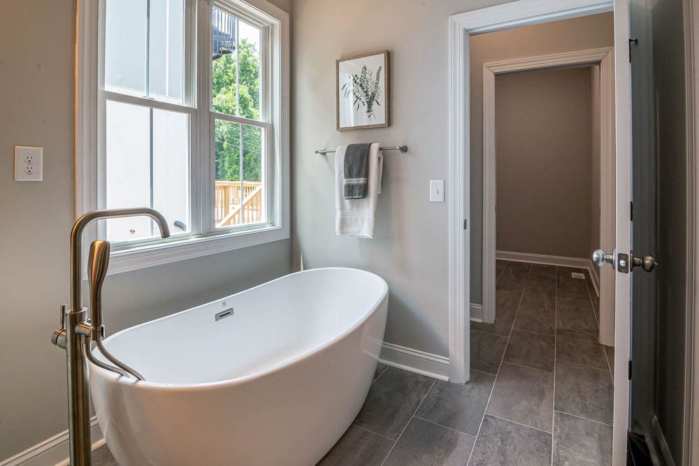 Freestanding tub with a brushed nickel floor-mounted filler and hand shower beside a double-hung window