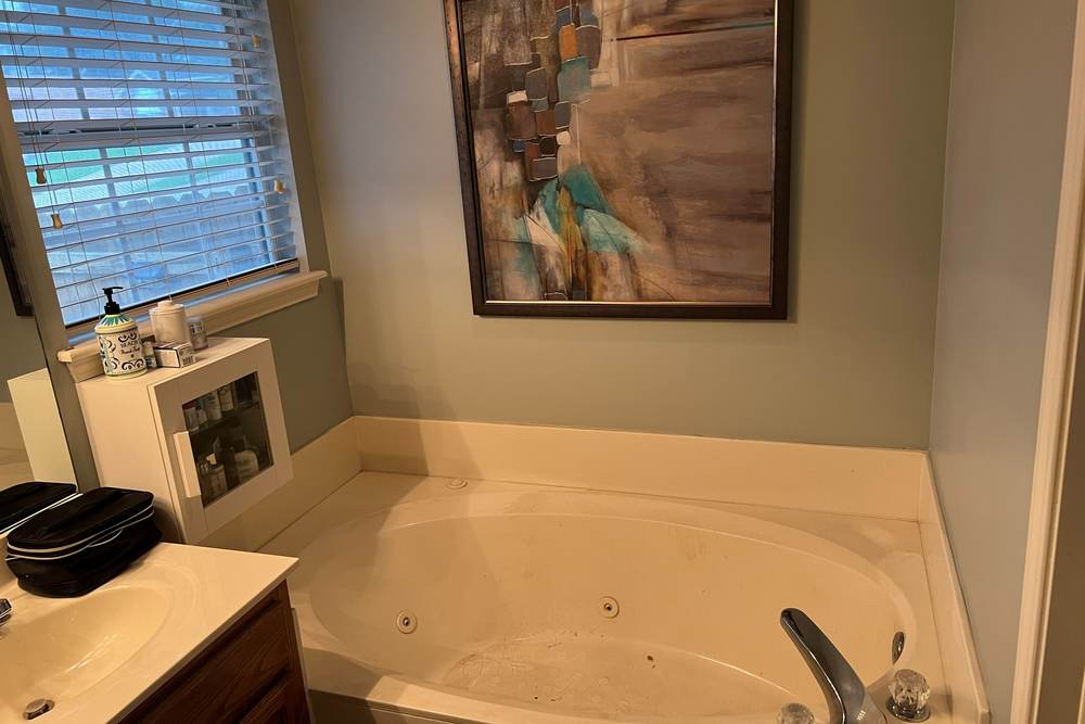 Before: a jetted garden tub under a window beside an oak vanity, in the east Tulsa master bathroom we remodeled