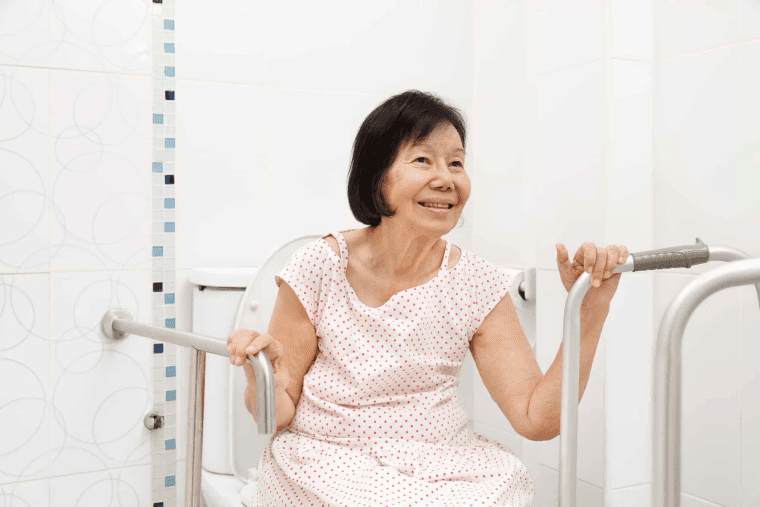 Older woman holding bathroom grab bars beside a toilet
