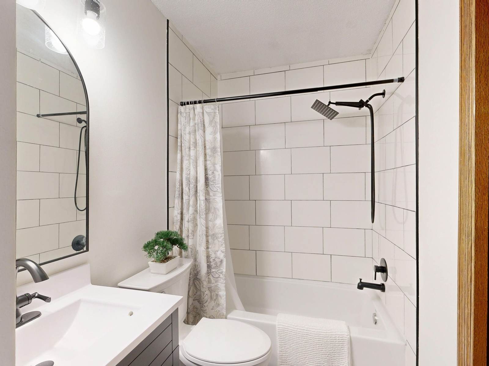 Small hall bathroom with large white subway tile around a tub and shower, a black rain head and a gray vanity