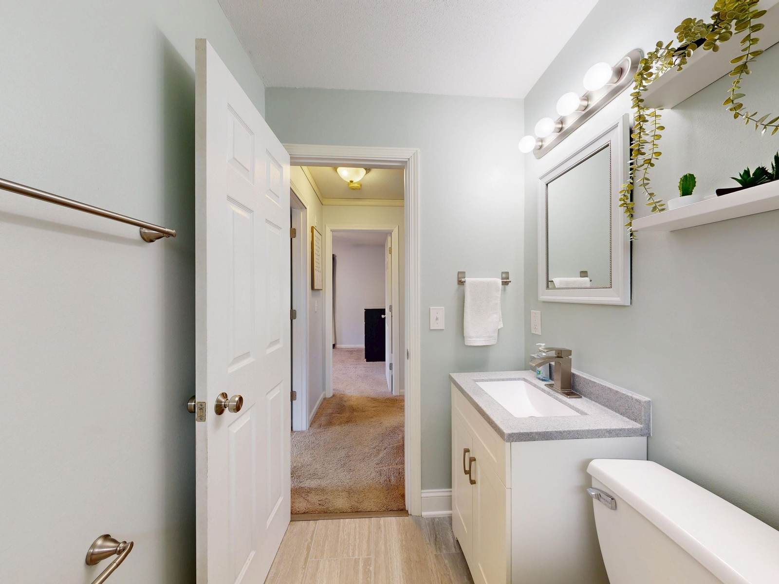 Narrow hall bathroom with a single white vanity, a speckled gray top with a rectangular sink and a brushed nickel faucet beside the toilet