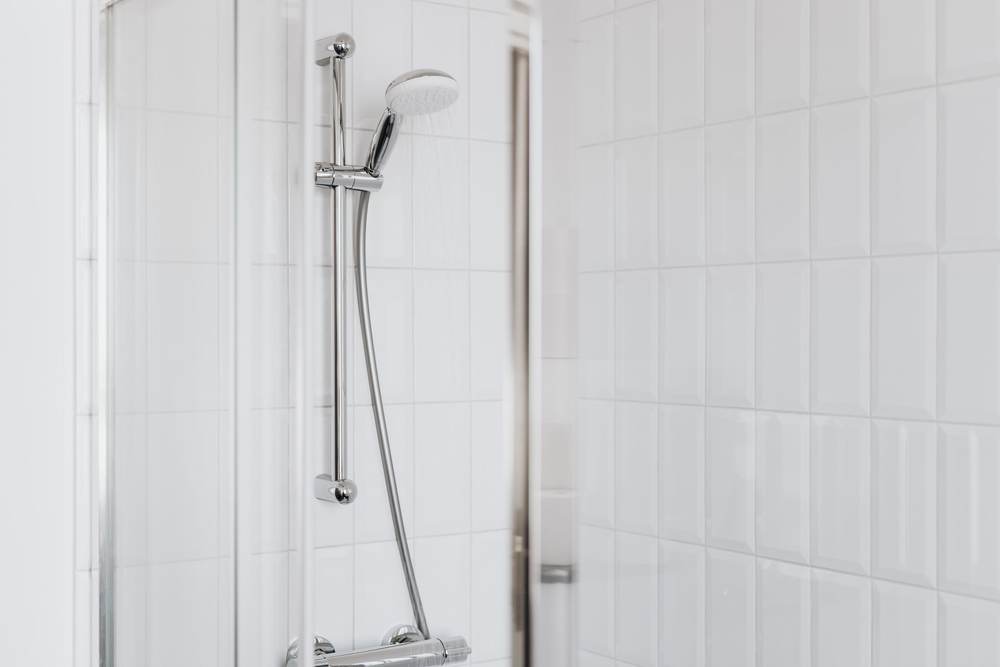 Hand shower on a vertical slide bar with a lever control, on white wall tile