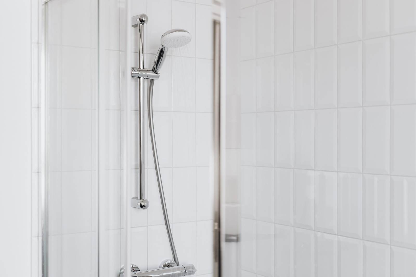 Hand shower on a chrome slide bar above an exposed shower mixer on white tile