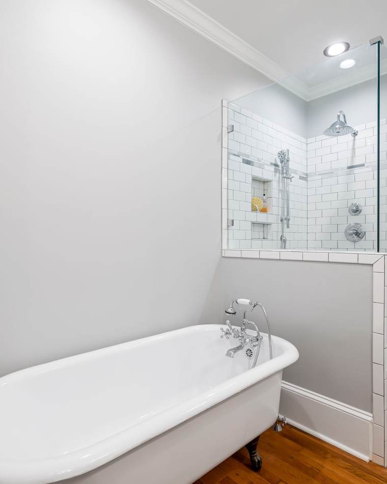 Clawfoot tub on a wood floor beside a new white subway tile shower with a glass door, a rain head and a hand shower