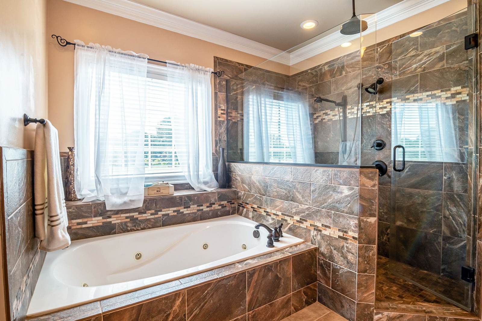 Primary bathroom with a jetted tub in a brown tile surround beside a tiled shower behind a glass door