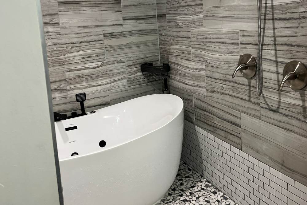 Handheld shower and valve on the tiled wall beside a freestanding tub, both inside one waterproofed wet room in a south Tulsa home we remodeled