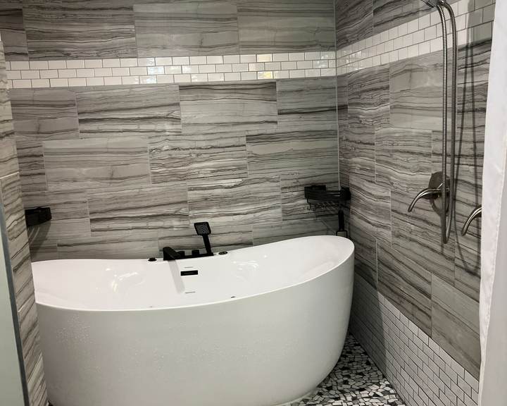 Freestanding soaking tub in a tiled wet room with a pebble floor and a white subway tile band, in a south Tulsa home
