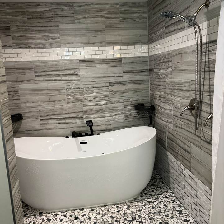 A freestanding soaking tub in a tiled wet room with a pebble mosaic floor and a white subway tile band