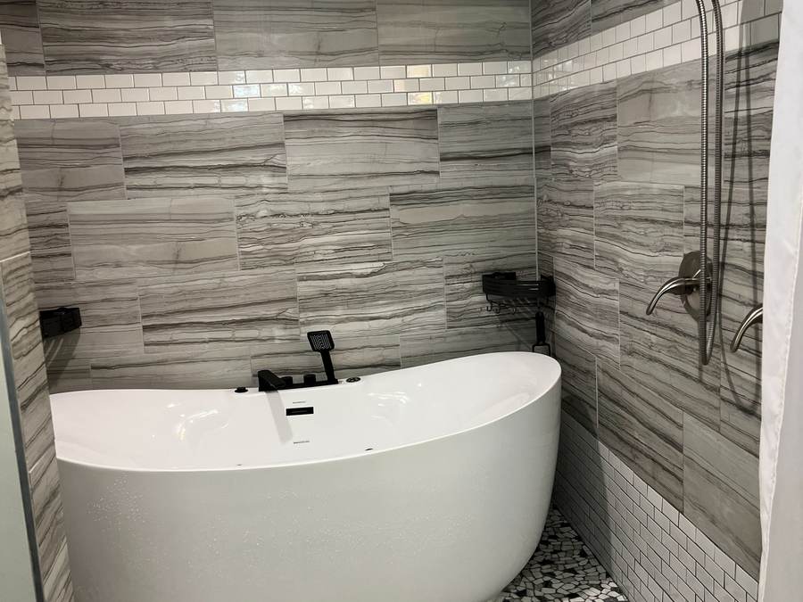 Freestanding soaking tub in a tiled wet room with a pebble floor and a white subway tile band, in a south Tulsa home